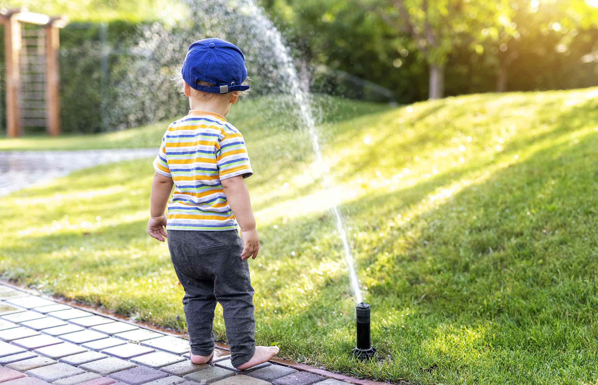 young boy looking at automatic sprinklers irrigating a front yard lawn