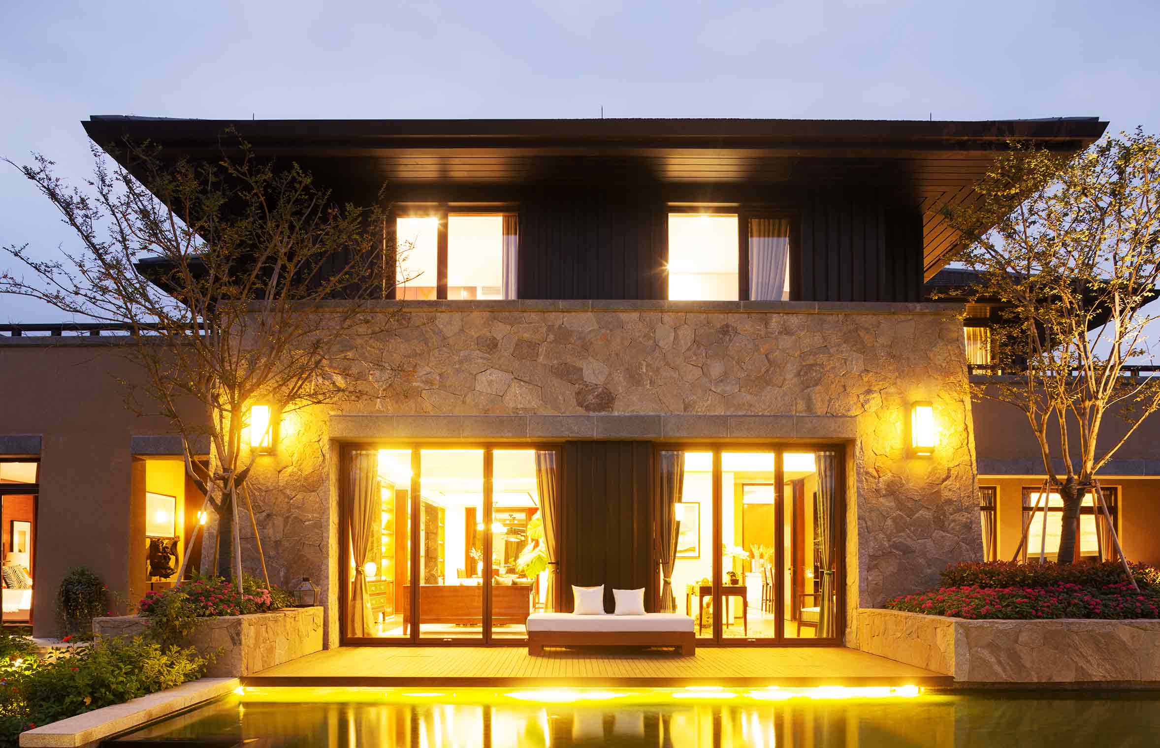 beautiful stone clad home with outdoor lighting and reflective pool